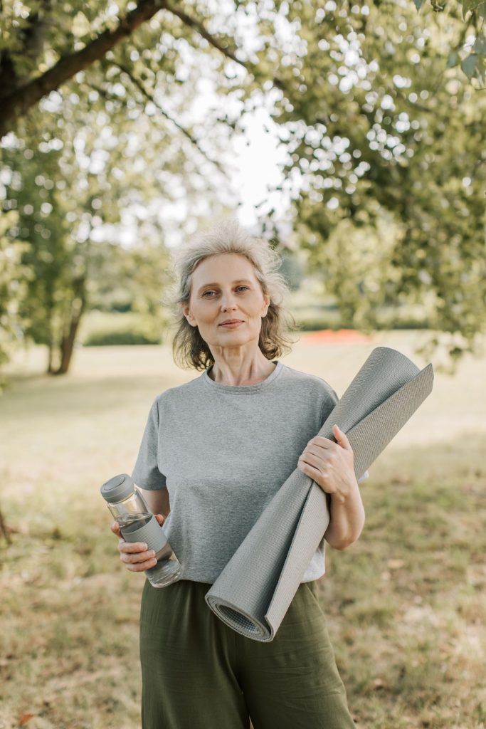 Donna matura con tappetino da yoga e borraccia in un parco: movimento e prevenzione per la salute delle ossa